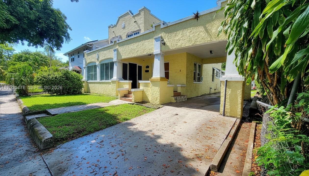 A yellow stucco house features a front porch, a concrete driveway, and a small lawn — MIAMI, FL