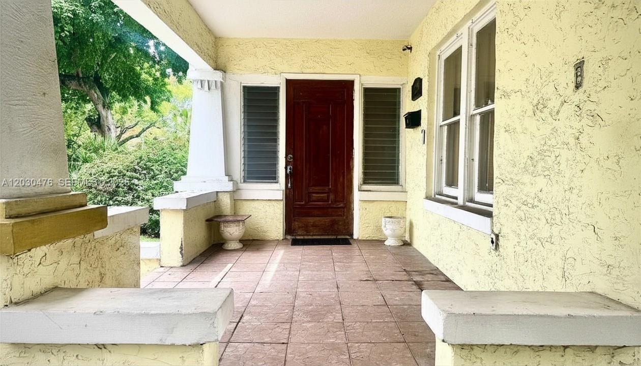 A covered front porch features a wooden door, tiled flooring, and stucco walls — MIAMI, FL