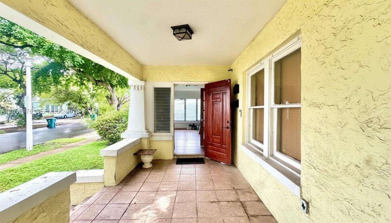 A covered front porch with tiled flooring leads to an open wooden front door — MIAMI, FL