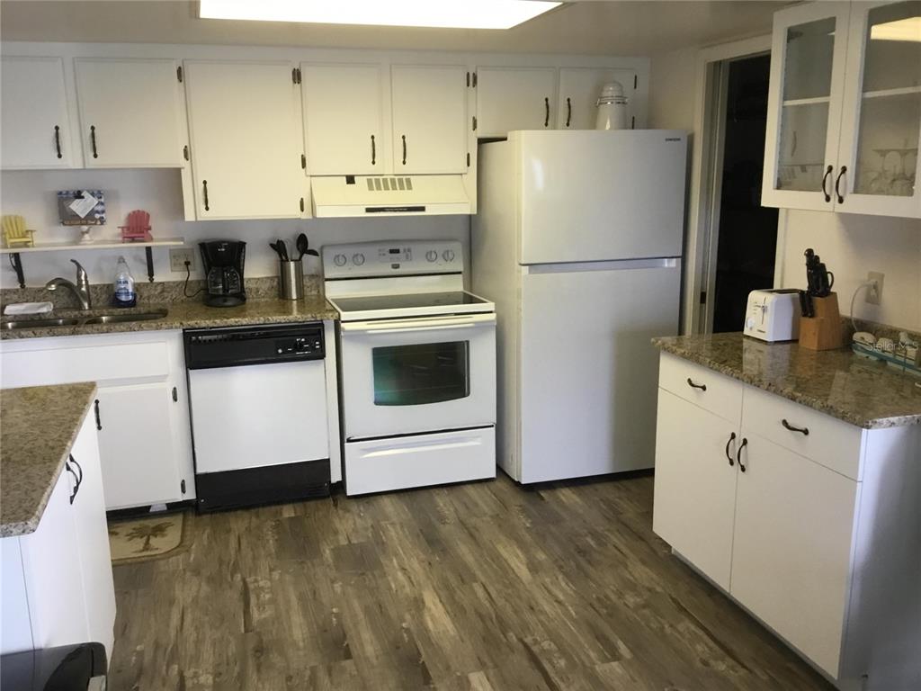 A kitchen features white cabinetry, granite countertops, white appliances, and wood-look flooring — 1571 S ATLANTIC AVENUE UNIT 412, NEW SMYRNA BEACH, FL