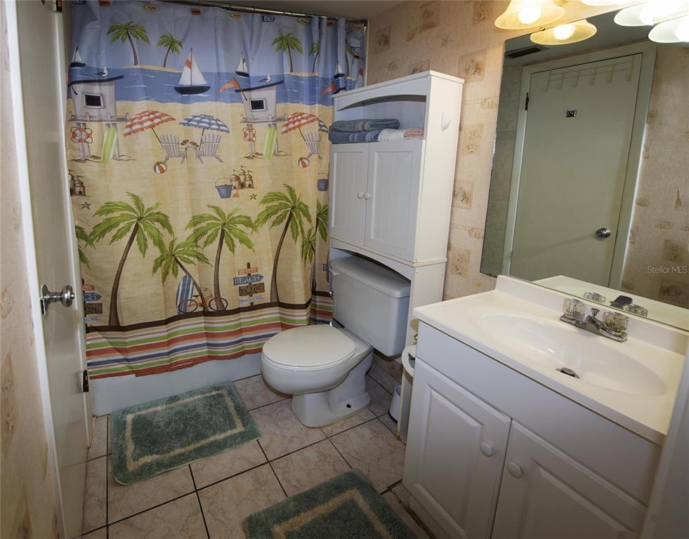 A bathroom features a beach-themed shower curtain, a white toilet with storage, and a vanity — 1571 S ATLANTIC AVENUE UNIT 412, NEW SMYRNA BEACH, FL