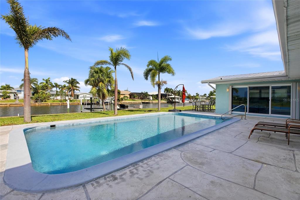 A swimming pool sits on a patio next to a house overlooking a canal — 174 SEVERIN ROAD SE, PORT CHARLOTTE, FL