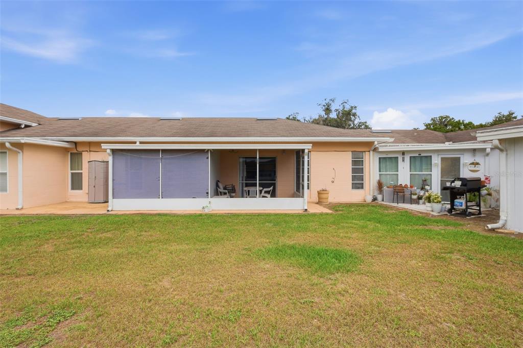 The backyard of a single-story house features a screened-in patio and a grassy lawn — 2629 CLUB CIRCLE UNIT 2629, LAKE WALES, FL