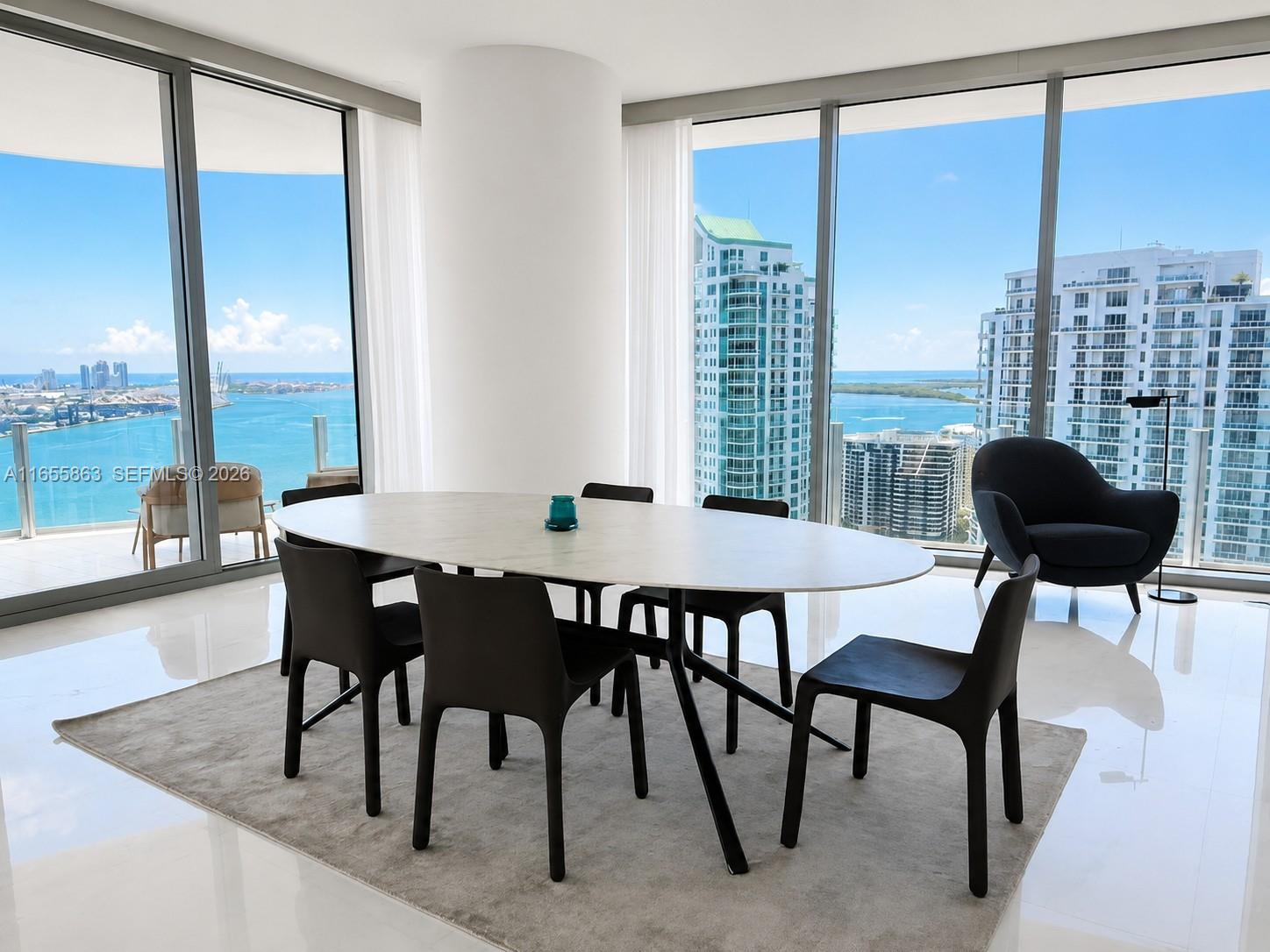 A dining room with an oval table, modern chairs, and floor-to-ceiling windows overlooking the ocean — 300 Biscayne Blvd Way # 3201, Miami FL 33131, MIAMI, FL