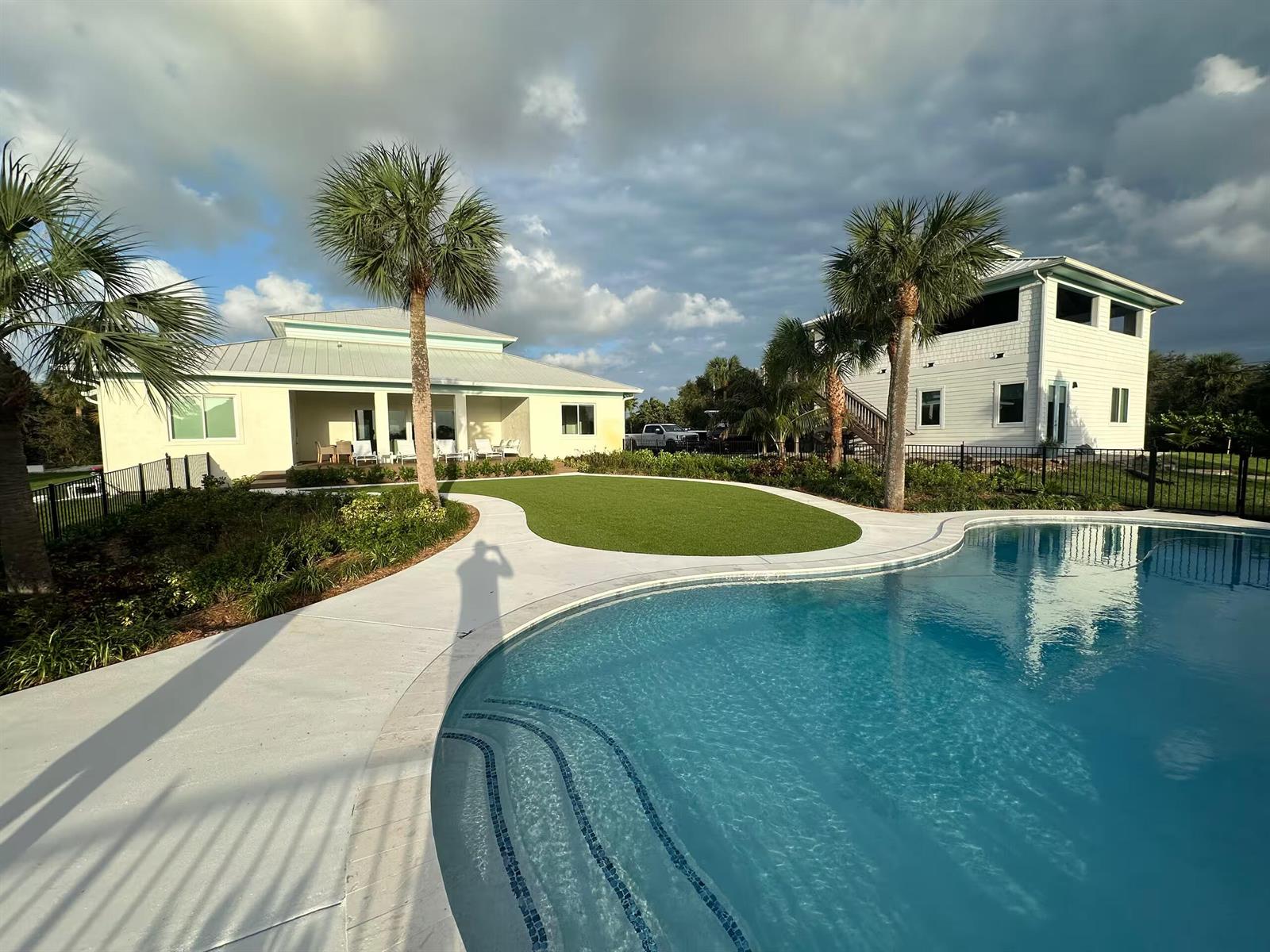 A swimming pool sits in front of a lawn and two houses under a cloudy sky — 12331 S Indian River Drive, Jensen Beach FL 34957, JENSEN BEACH, FL