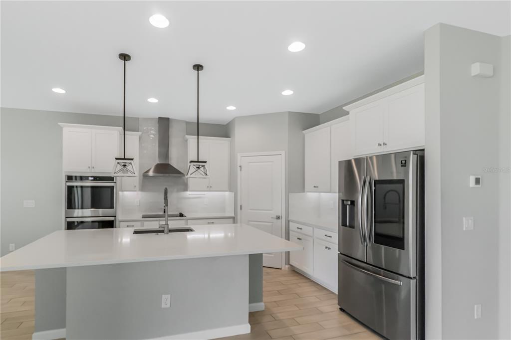 A modern kitchen features white cabinetry, a large island with a sink, and stainless appliances — 30053 ISLAND CLUB DRIVE, DEER ISLAND, FL