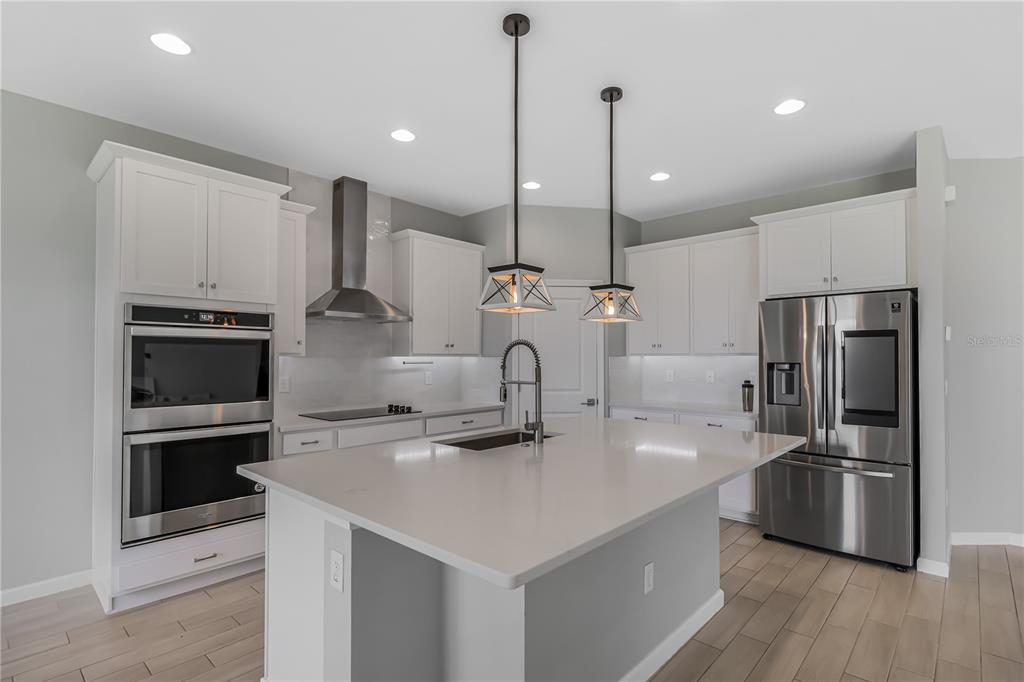 A modern kitchen features white cabinetry, stainless steel appliances, a quartz island, and pendant lighting — 30053 ISLAND CLUB DRIVE, DEER ISLAND, FL