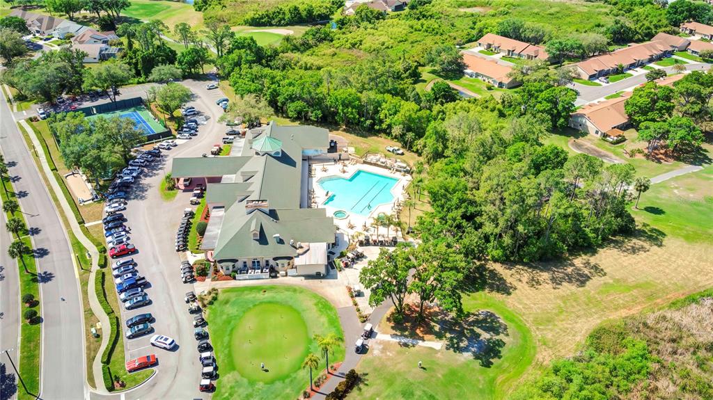 An aerial view shows a clubhouse with a swimming pool, parking lot, and putting green — 6447 PINE WALK DRIVE, NEW PORT RICHEY, FL