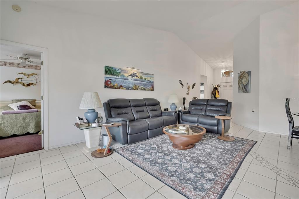 A living room features gray leather sofas, a patterned area rug, and tile flooring — 6447 PINE WALK DRIVE, NEW PORT RICHEY, FL