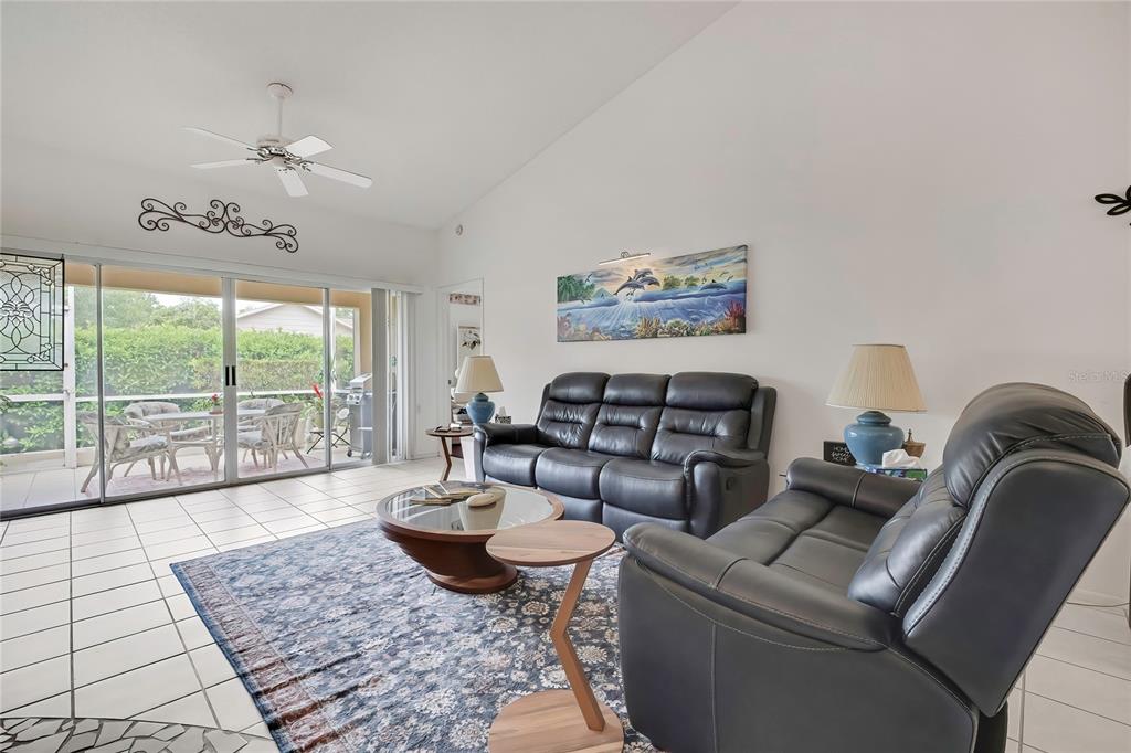 A living room features dark leather sofas, a glass-topped coffee table, and sliding glass doors — 6447 PINE WALK DRIVE, NEW PORT RICHEY, FL