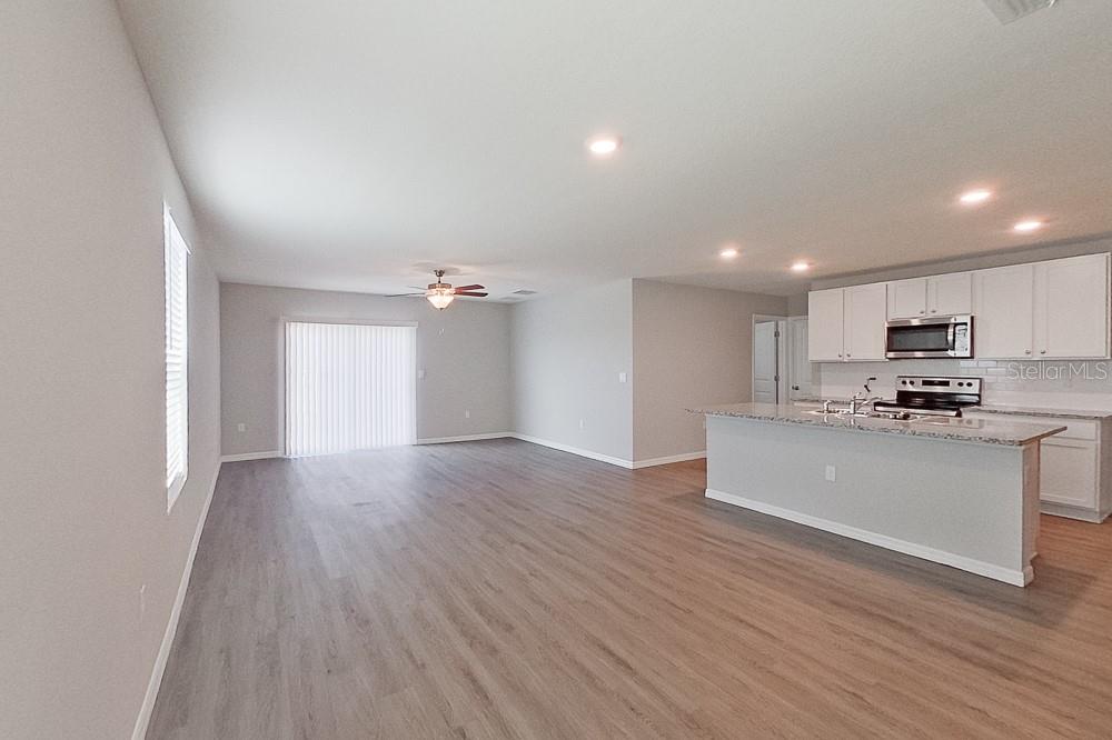 An open-concept living area features light wood-look flooring, a kitchen island, and white cabinetry — 8740 SW 43RD TERRACE, OCALA, FL