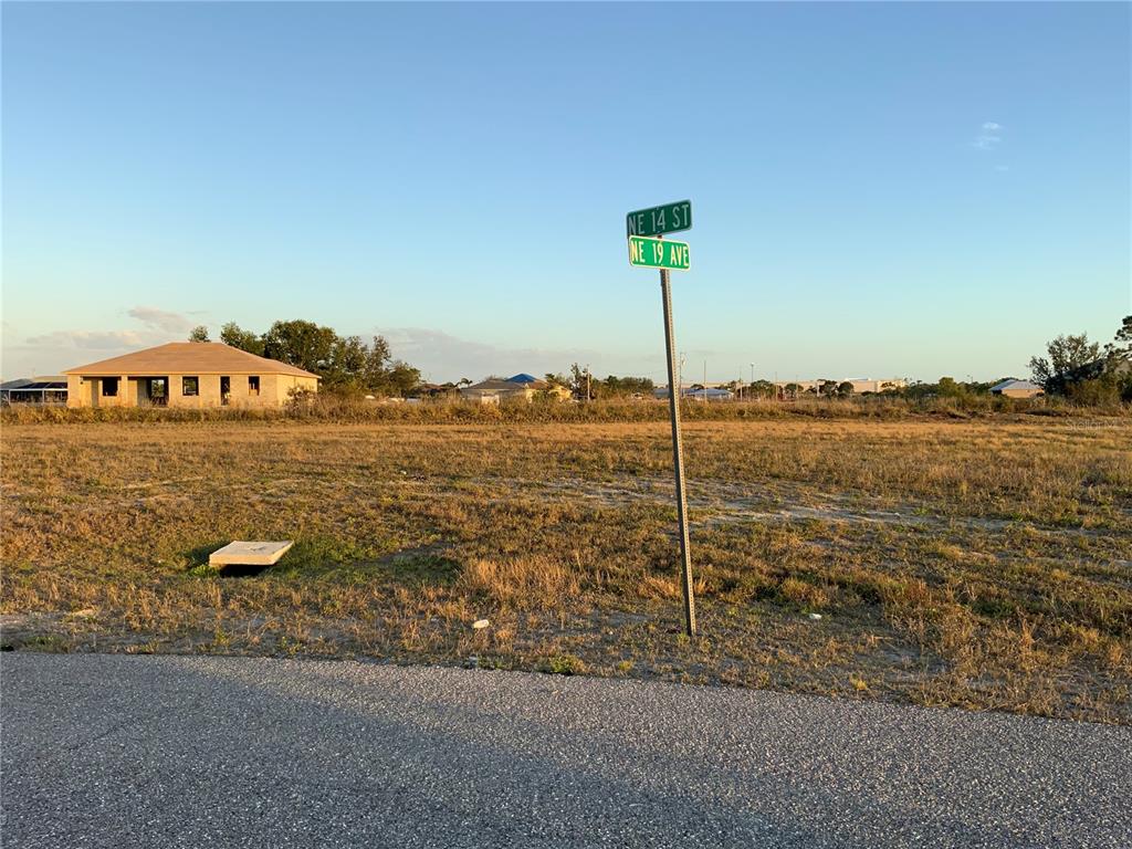 A vacant, grassy lot at the corner of a street with a road sign — 1830 NE 14TH STREET, CAPE CORAL, FL