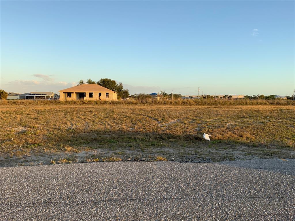 A vacant, grassy lot sits in front of a house under construction — 1830 NE 14TH STREET, CAPE CORAL, FL