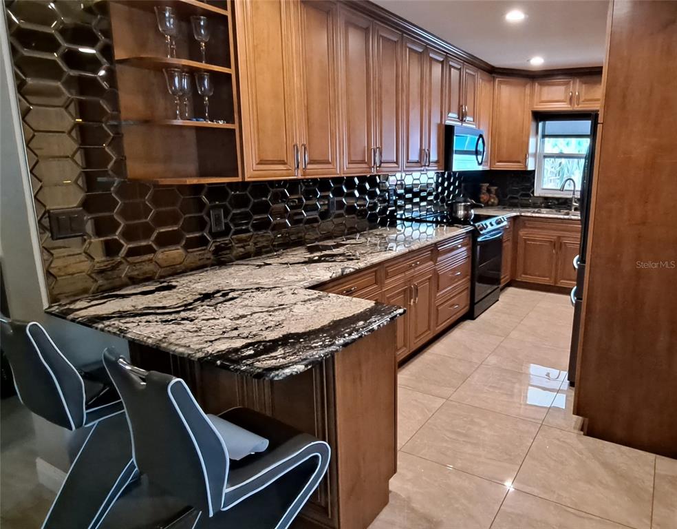 A kitchen features wood cabinets, black and white granite countertops, and a hexagonal tile backsplash — 3964 22ND AVENUE N, ST PETERSBURG, FL