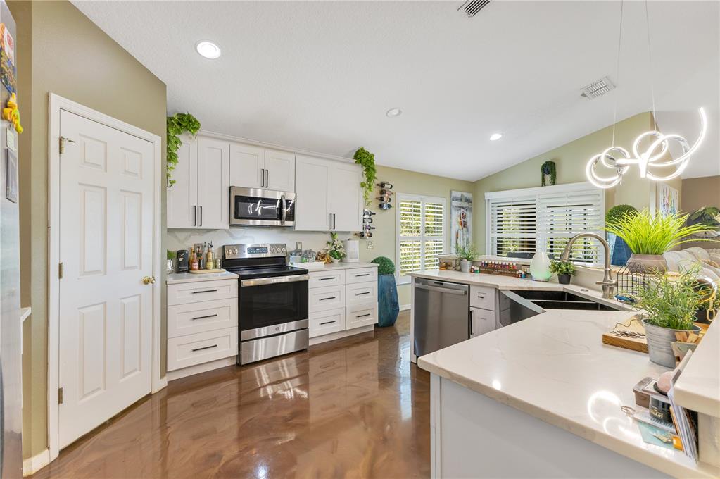 A kitchen features white cabinets, stainless steel appliances, a kitchen island, and glossy brown flooring — 2717 EAGLE CANYON DRIVE S, KISSIMMEE, FL