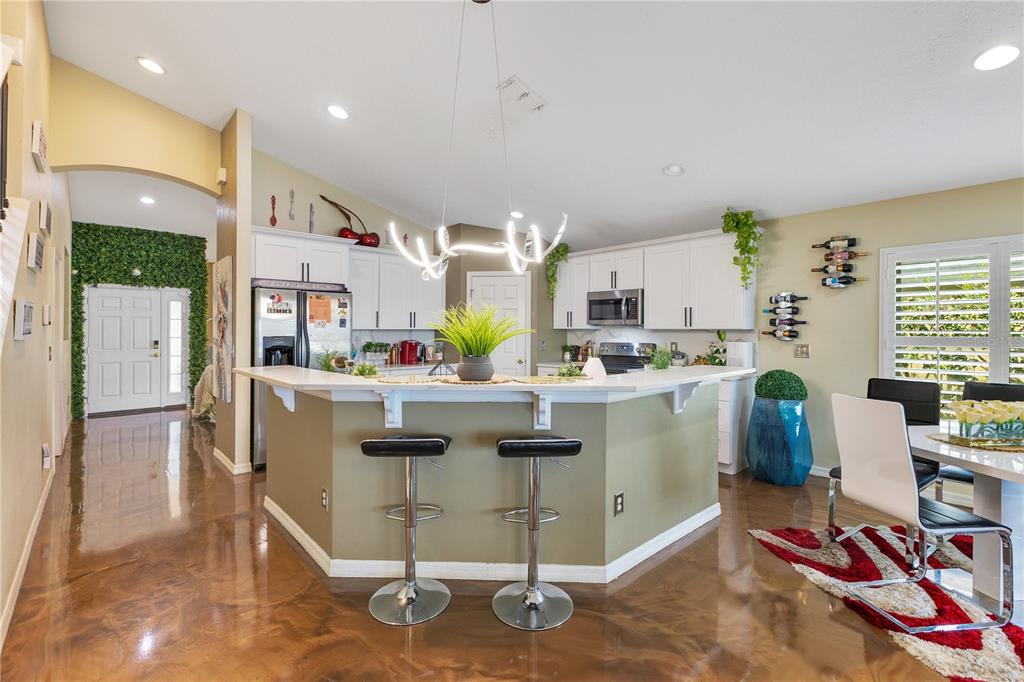 A kitchen features white cabinets, a peninsula with bar stools, and polished brown flooring — 2717 EAGLE CANYON DRIVE S, KISSIMMEE, FL