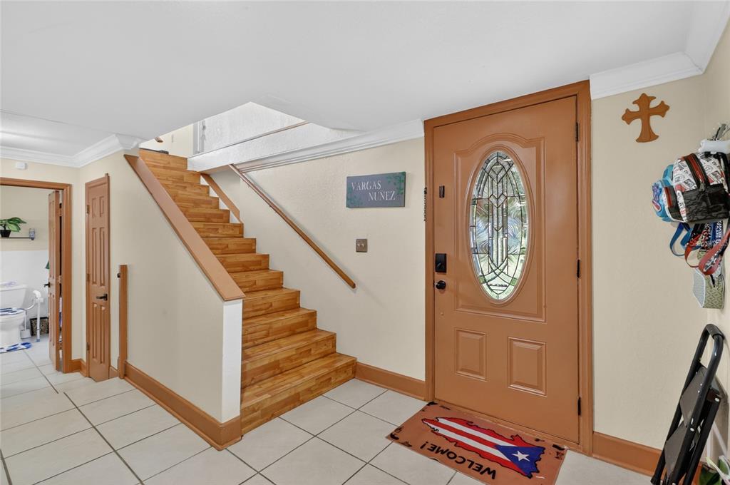 An entryway features a wooden staircase, a brown front door, and a Puerto Rican flag mat — 3126 TOOLE ROAD, LITHIA, FL