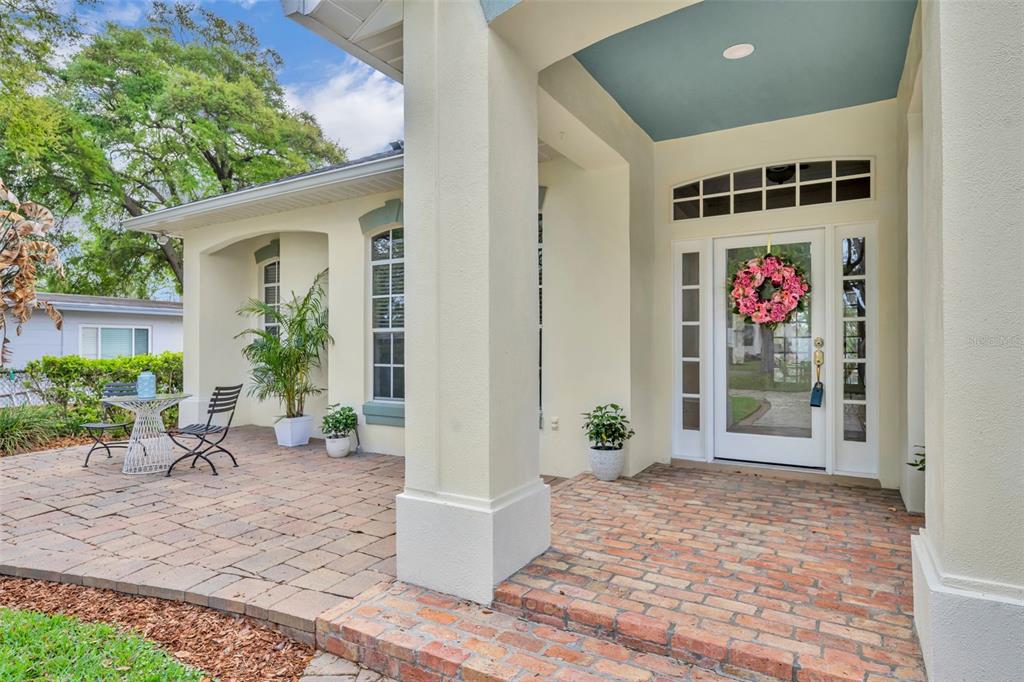 A brick patio leads to a white front door with a wreath under a covered porch — 1800 MAGNOLIA AVENUE, WINTER PARK, FL