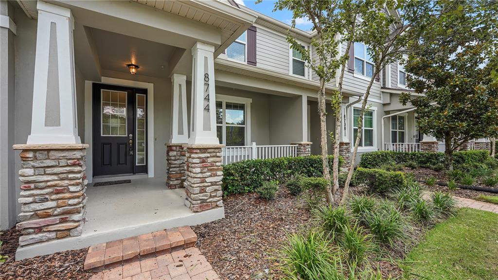The exterior of a multi-story townhouse features a covered porch with stone-based columns and siding — 8744 DUFFERIN LANE, ORLANDO, FL