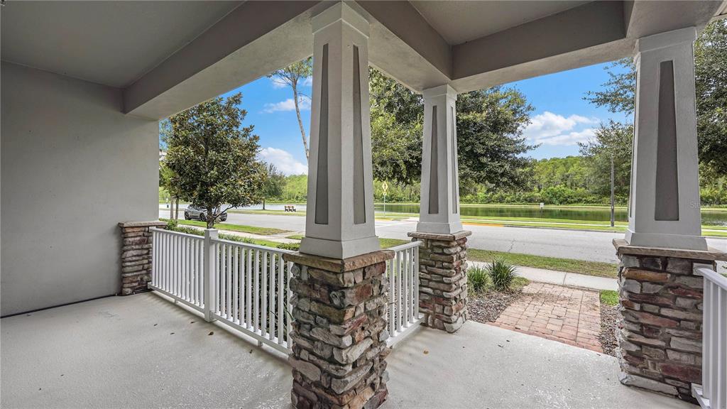 A covered porch features stone-based columns, a white railing, and a view of a lake — 8744 DUFFERIN LANE, ORLANDO, FL