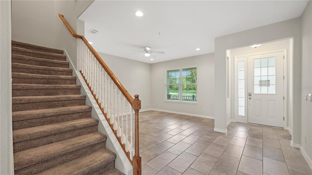 An entryway features a carpeted staircase with a wooden railing and light-colored tile flooring — 8744 DUFFERIN LANE, ORLANDO, FL