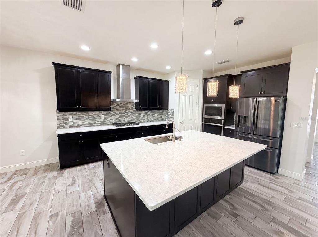A modern kitchen features dark cabinets, a large white quartz island, and stainless steel appliances — 21797 BRISKE MORNING AVENUE, LAND O LAKES, FL