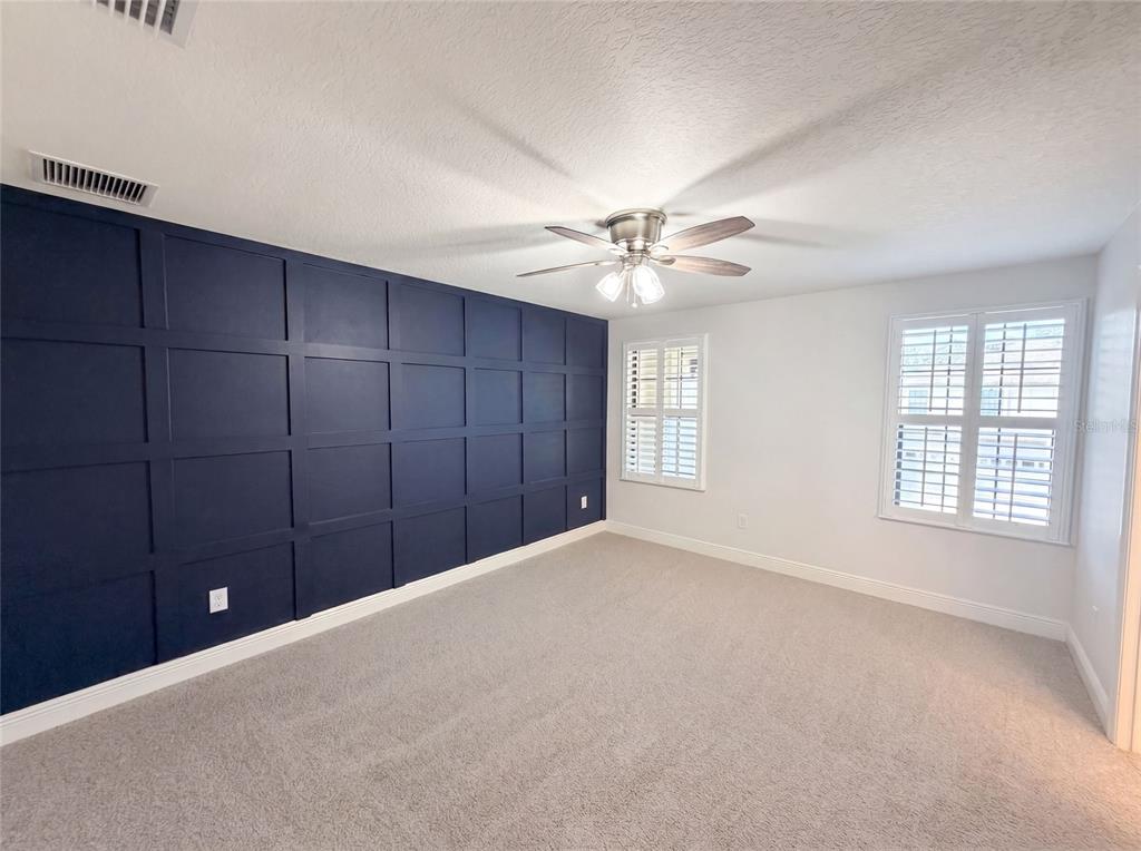 A bedroom features a dark blue grid-paneled accent wall, gray carpeting, and white plantation shutters — 21797 BRISKE MORNING AVENUE, LAND O LAKES, FL