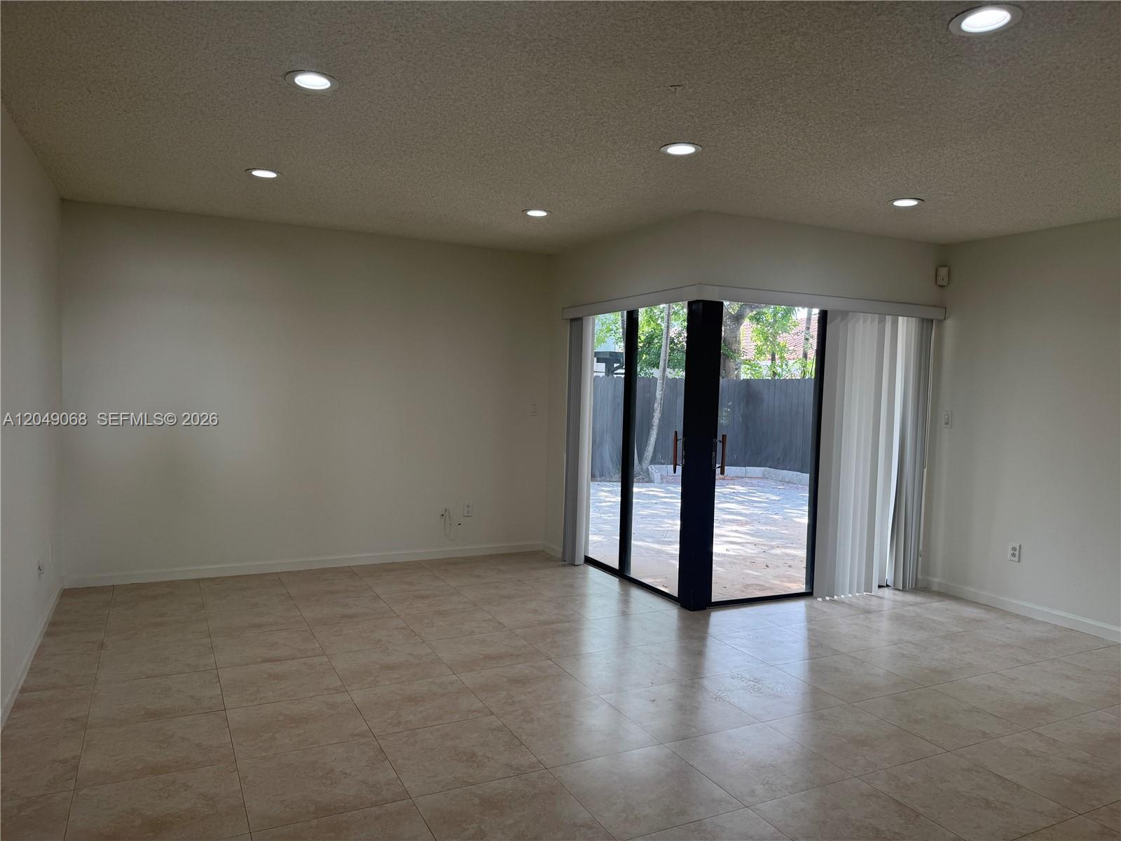 A bright, empty living room features beige tile flooring, recessed lighting, and sliding glass doors — 15054 SW 127th Pl # 0, Miami FL 33186, MIAMI, FL