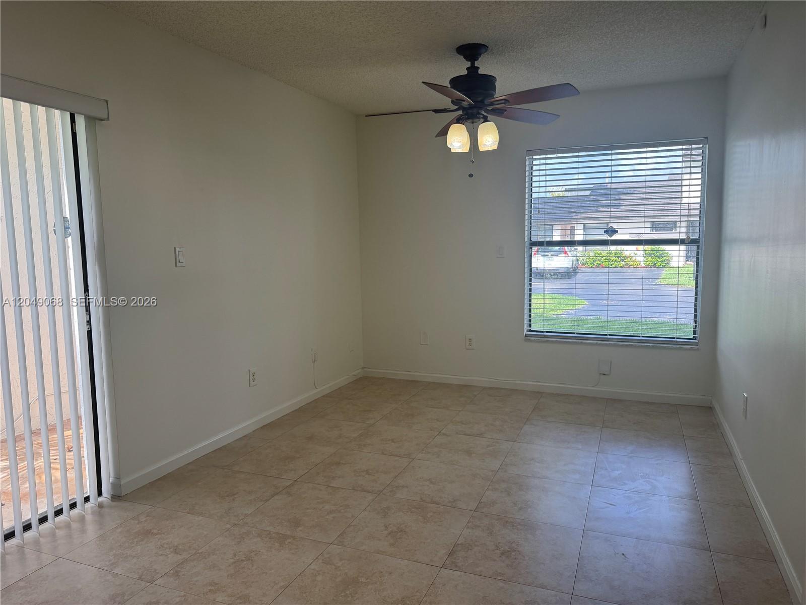 An empty room features beige tile flooring, a ceiling fan, and a large window — 15054 SW 127th Pl # 0, Miami FL 33186, MIAMI, FL
