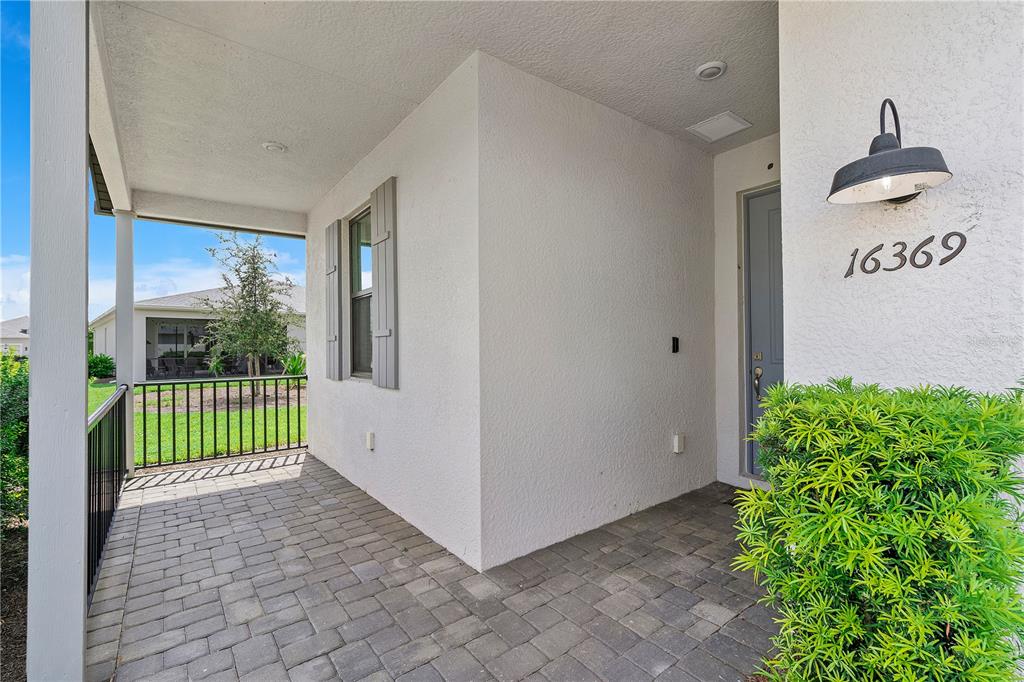 A paved entryway porch features a white stucco wall, a gray door, and a light fixture — 16369 PALMETTO STREET, PUNTA GORDA, FL
