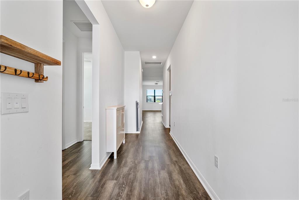 A hallway with wood-look flooring leads to a bright room with a window — 16369 PALMETTO STREET, PUNTA GORDA, FL