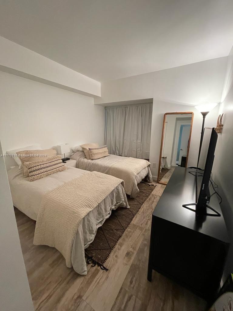 A bedroom features two twin beds, a black dresser with a television, and wood-look flooring — 650 NE 32nd St # 3606, Miami FL 33137, MIAMI, FL