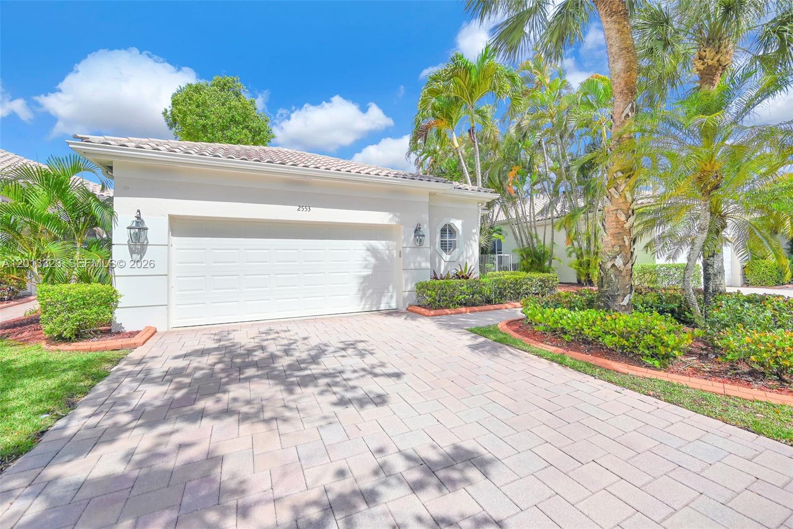 A single-story house features a white garage, a paved driveway, and surrounding palm trees — 2553 Bay Pointe Drive, Weston FL 33327, WESTON, FL