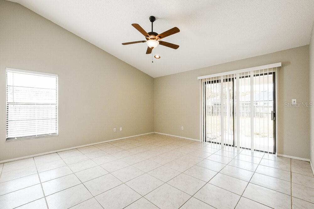 An empty room with light-colored tile flooring, a vaulted ceiling, and sliding glass doors — 1000 DINERO DRIVE, WINTER SPRINGS, FL