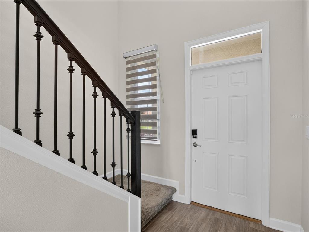 An entryway features a white door with a transom window, stairs with black railings, and flooring — 1152 TRAPPERS TRAIL LOOP, DAVENPORT, FL