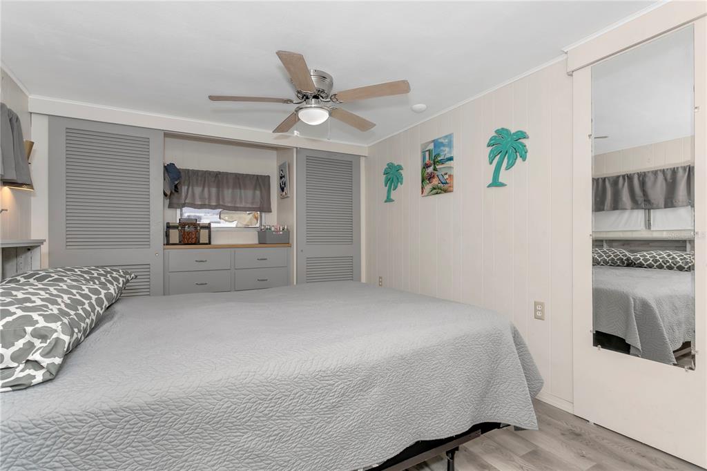 A bedroom features a gray bed, louvered closet doors, a ceiling fan, and wall decor — 5127 8TH STREET W, BRADENTON, FL