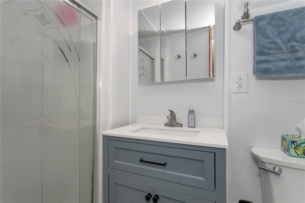 A bathroom features a gray vanity with a white countertop, a medicine cabinet, and a shower — 5127 8TH STREET W, BRADENTON, FL