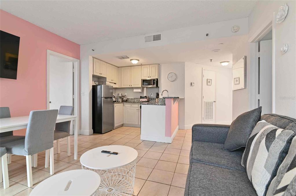 An open-concept living room and kitchen area with tile flooring, pink walls, and gray furniture — 6165 CARRIER DRIVE UNIT 1402, ORLANDO, FL