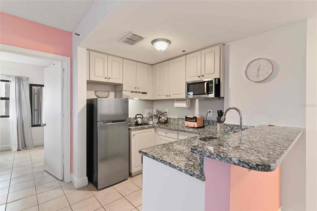 A kitchen features white cabinets, granite countertops, a stainless steel refrigerator, and a breakfast bar — 6165 CARRIER DRIVE UNIT 1402, ORLANDO, FL