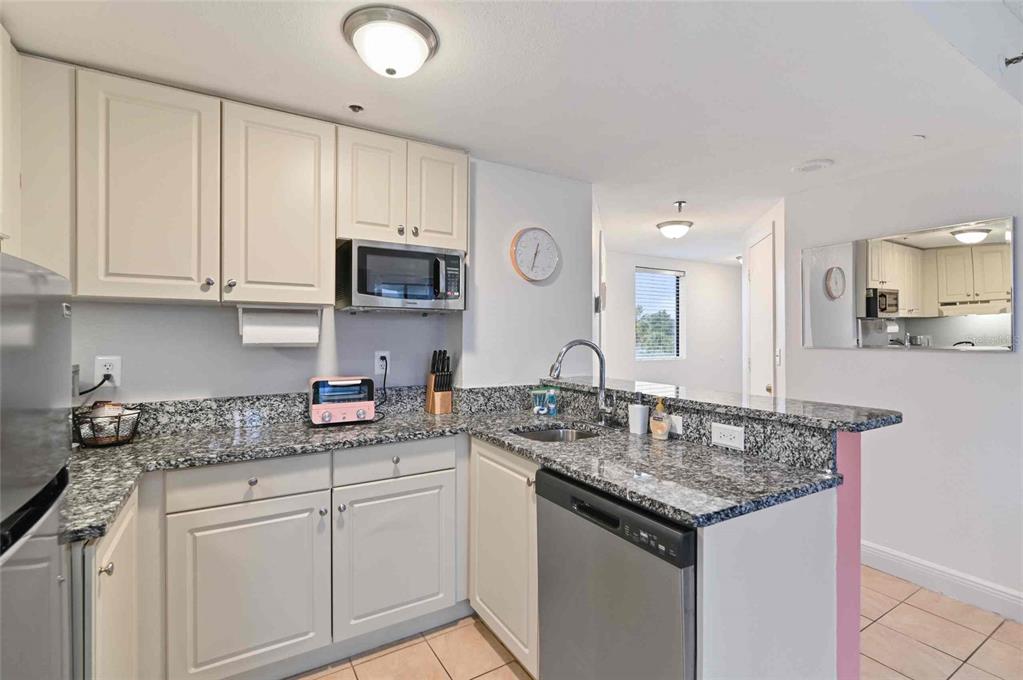 A kitchen features light-colored cabinets, granite countertops, stainless steel appliances, and tile flooring — 6165 CARRIER DRIVE UNIT 1402, ORLANDO, FL