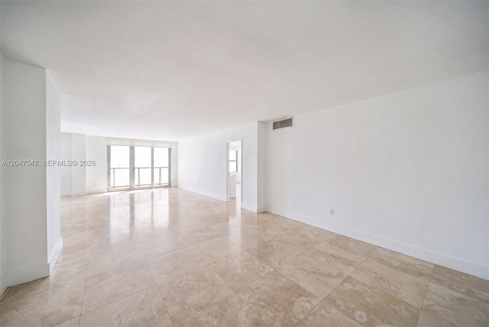 A spacious, empty living room features white walls, large beige floor tiles, and a balcony — 5701 Collins Ave # 1415, Miami Beach FL 33140, MIAMI BEACH, FL