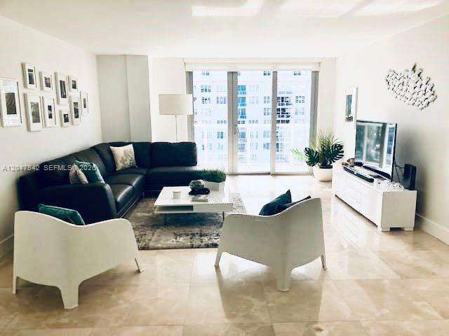 A modern living room features a dark sectional sofa, two white chairs, and a television — 5701 Collins Ave # 1415, Miami Beach FL 33140, MIAMI BEACH, FL