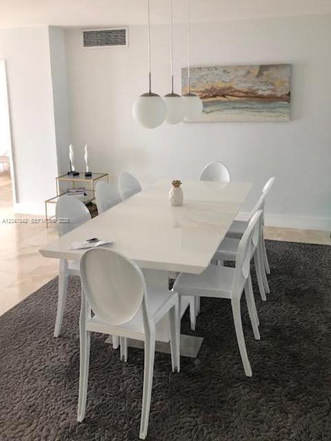 A modern dining room features a white table, six white chairs, and three globe pendant lights — 5701 Collins Ave # 1415, Miami Beach FL 33140, MIAMI BEACH, FL