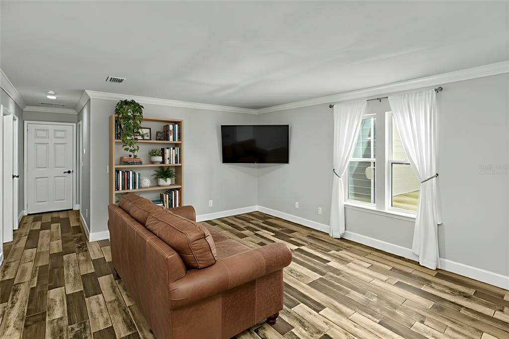 A living room features a brown leather sofa, a wooden bookshelf, and a wall-mounted television — 11751 NE 105TH AVENUE, ARCHER, FL