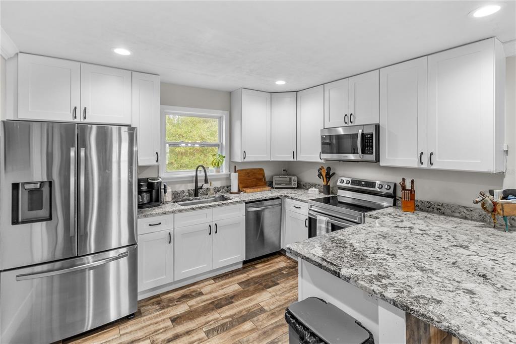 A kitchen with white cabinets, granite countertops, stainless steel appliances, and wood-look flooring — 11751 NE 105TH AVENUE, ARCHER, FL