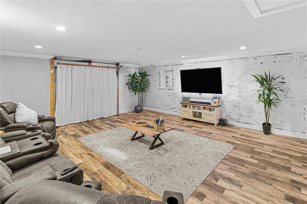 A living room features wood-look flooring, a white brick accent wall, and a gray sectional sofa — 11751 NE 105TH AVENUE, ARCHER, FL