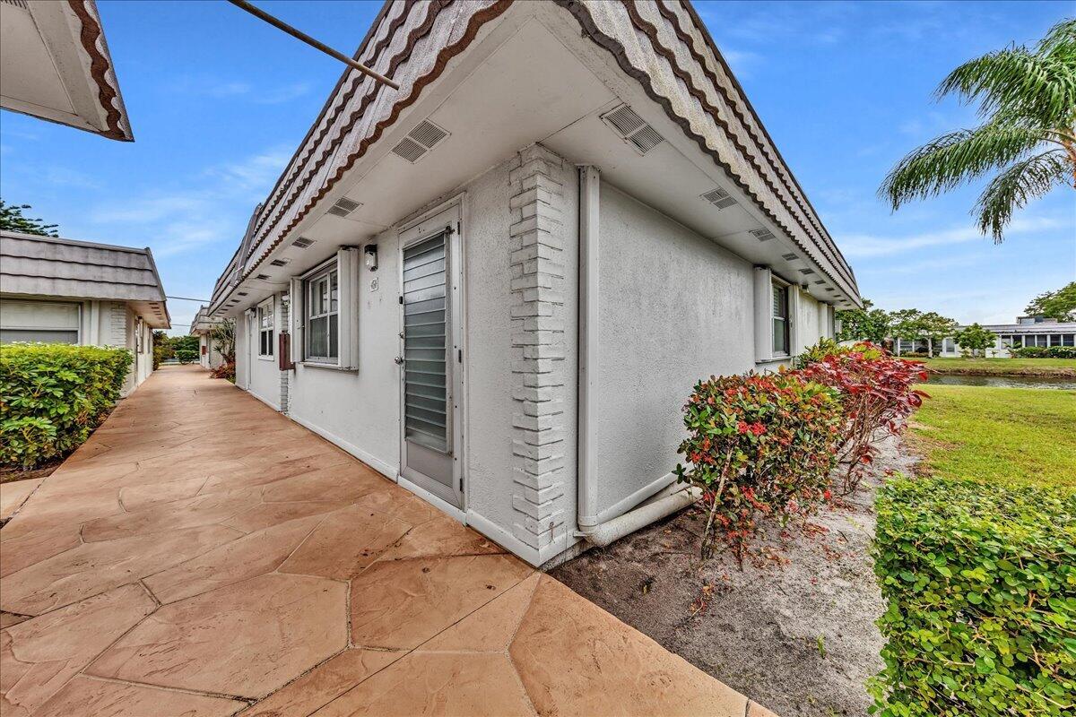 A view of a white exterior wall with a door and a stone-paved walkway — 150 Valencia Boulevard # G, Delray Beach FL 33446, DELRAY BEACH, FL