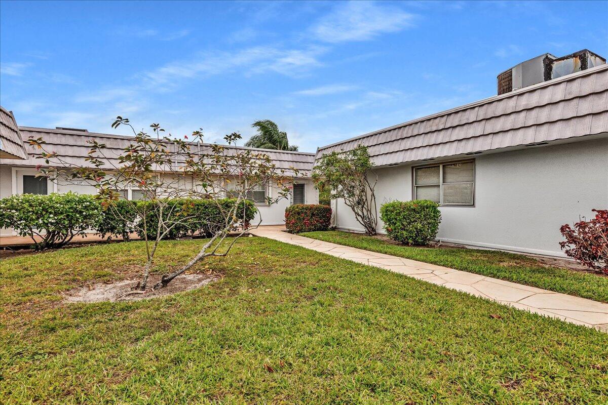 A walkway leads between two single-story residential buildings with light-colored walls and tiled roofs — 150 Valencia Boulevard # G, Delray Beach FL 33446, DELRAY BEACH, FL