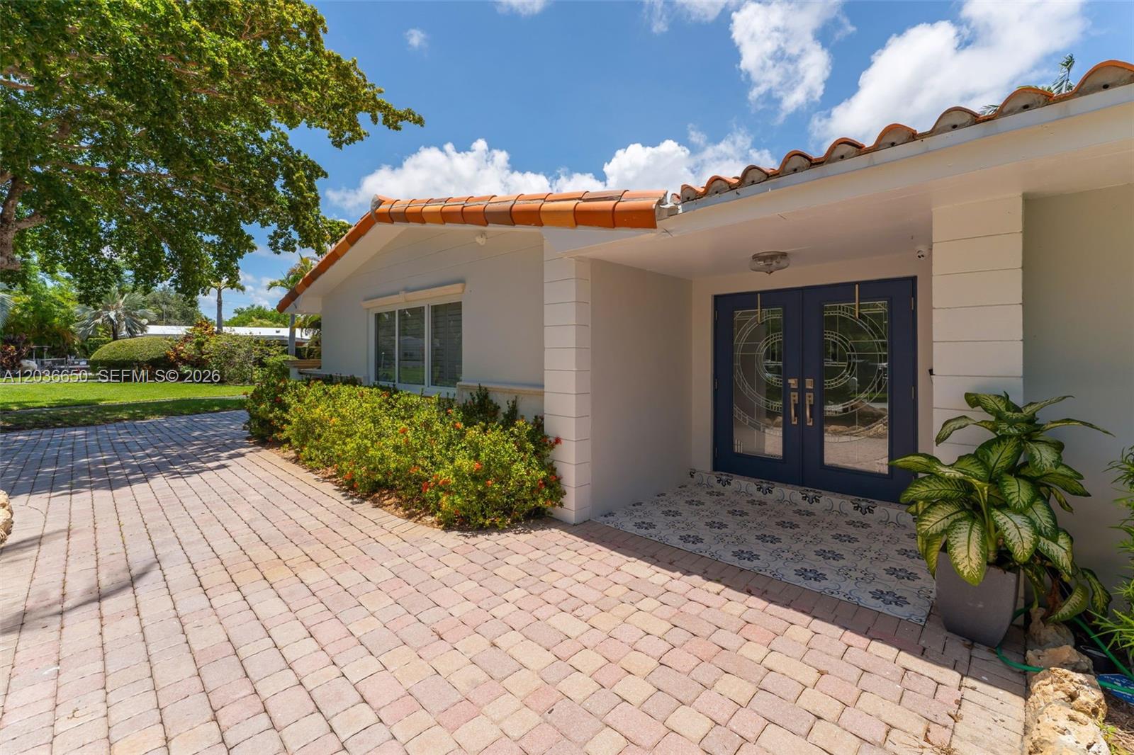 The exterior of a house features a tiled roof, double blue doors, and a paved driveway — 6561 Marlin Dr, Coral Gables FL 33158, CORAL GABLES, FL