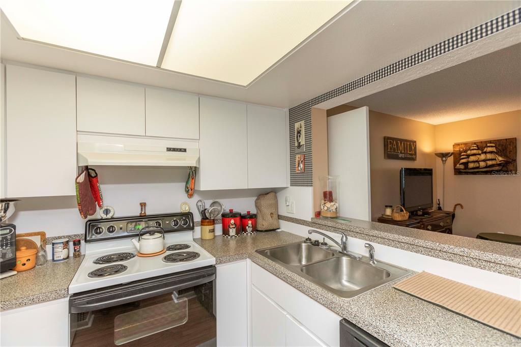 A kitchen features white cabinets, a white electric stove, and a stainless steel double sink — 4726 MARINE PARKWAY UNIT 201, NEW PORT RICHEY, FL